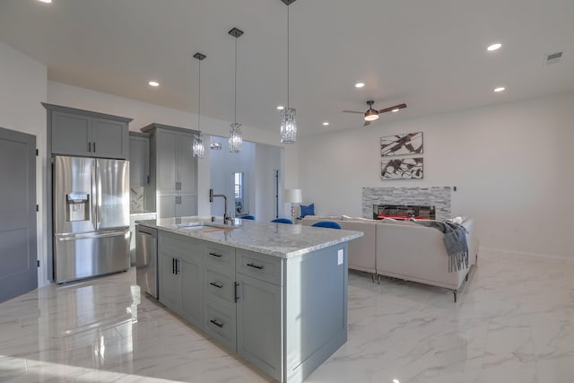 kitchen featuring gray cabinetry, stainless steel appliances, a kitchen island with sink, ceiling fan, and sink