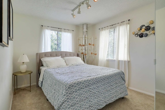 carpeted bedroom with a textured ceiling, track lighting, and multiple windows