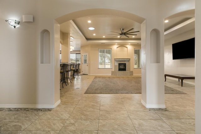 living room with a tiled fireplace, a tray ceiling, and ceiling fan