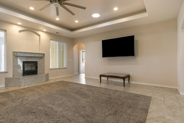 unfurnished living room featuring ceiling fan, a premium fireplace, a tray ceiling, and light tile patterned floors