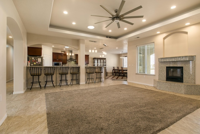 living room with a tray ceiling, a high end fireplace, ceiling fan, and light tile patterned flooring