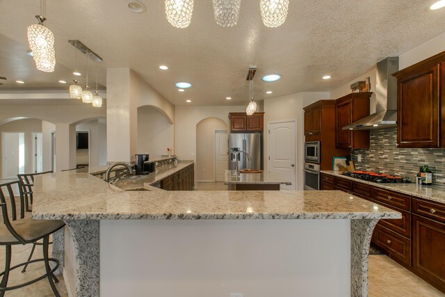 kitchen featuring appliances with stainless steel finishes, backsplash, light stone counters, wall chimney range hood, and a textured ceiling