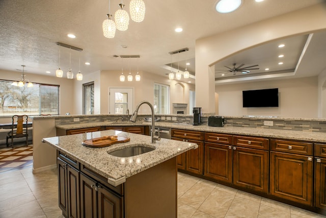 kitchen with pendant lighting, sink, ceiling fan, light stone countertops, and a large island with sink