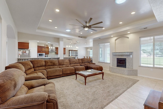 tiled living room with ceiling fan, a premium fireplace, and a tray ceiling