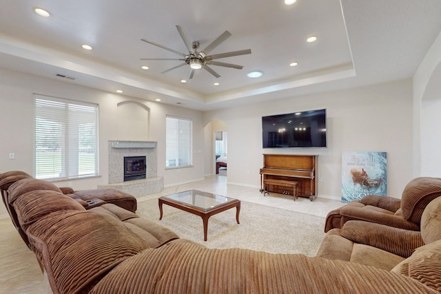 living room featuring ceiling fan, a premium fireplace, a tray ceiling, and light tile patterned floors