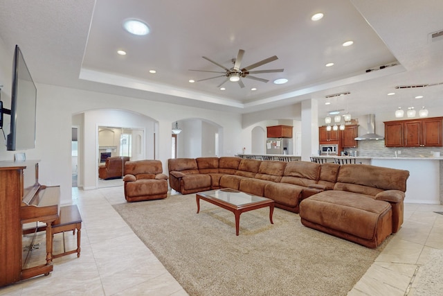 living room with light tile patterned floors, a raised ceiling, and ceiling fan