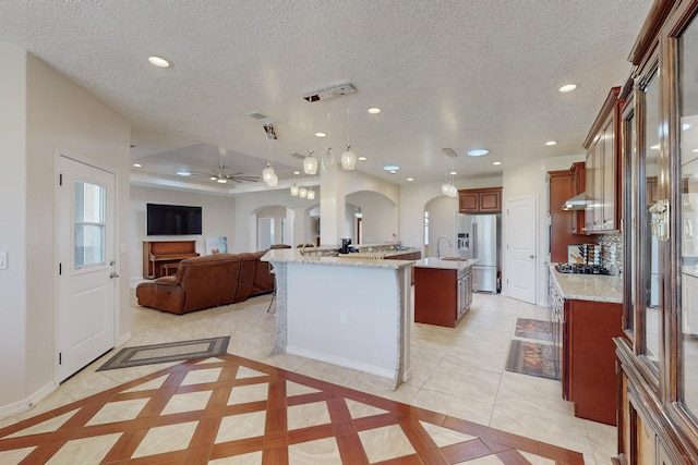 kitchen featuring appliances with stainless steel finishes, decorative light fixtures, an island with sink, light tile patterned floors, and a textured ceiling