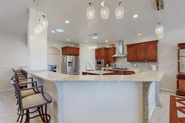 kitchen featuring wall chimney range hood, decorative light fixtures, stainless steel appliances, and a breakfast bar