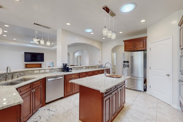 kitchen with hanging light fixtures, appliances with stainless steel finishes, sink, and a center island with sink