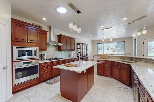 kitchen with pendant lighting, stainless steel appliances, sink, and wall chimney range hood