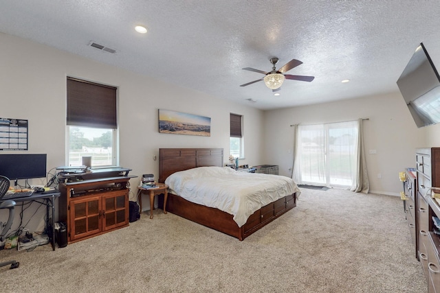 bedroom with multiple windows, ceiling fan, light colored carpet, and a textured ceiling