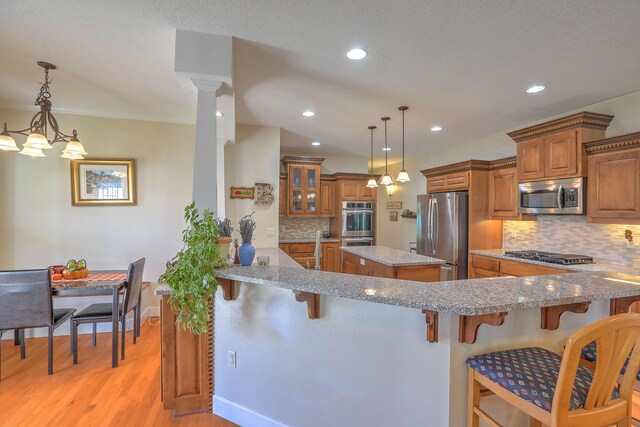 kitchen featuring a kitchen breakfast bar, hanging light fixtures, light hardwood / wood-style flooring, appliances with stainless steel finishes, and kitchen peninsula