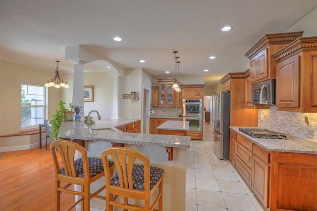 kitchen featuring appliances with stainless steel finishes, backsplash, ornate columns, an inviting chandelier, and a breakfast bar area