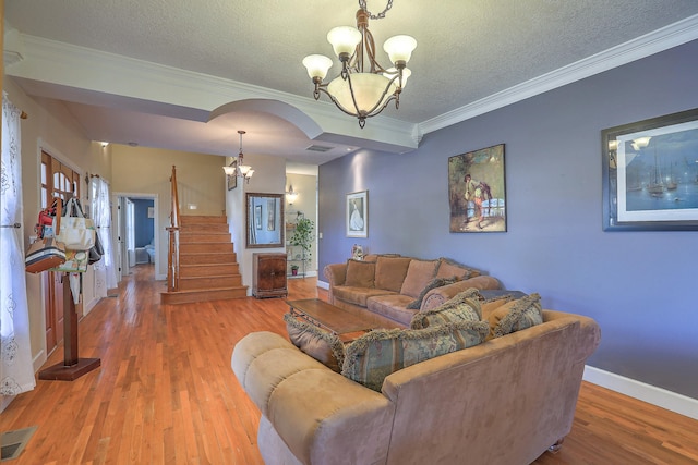 living room featuring an inviting chandelier, wood-type flooring, a textured ceiling, and ornamental molding