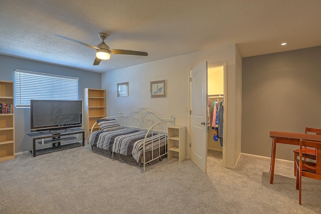 bedroom featuring light carpet, a walk in closet, a textured ceiling, ceiling fan, and a closet