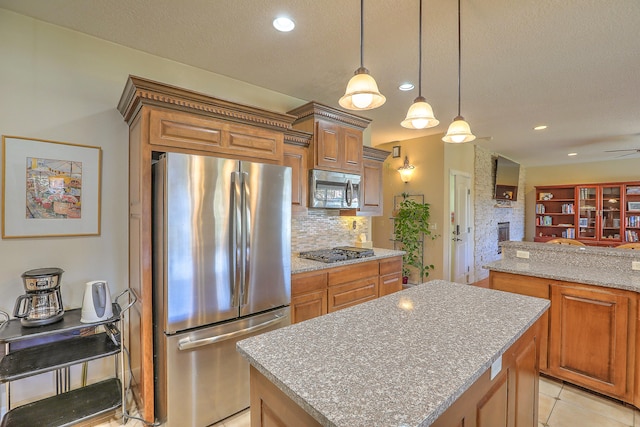 kitchen with ceiling fan, stainless steel appliances, a brick fireplace, pendant lighting, and a kitchen island