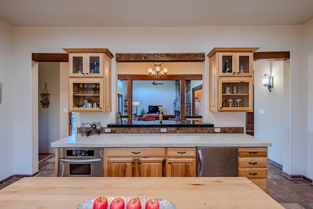 kitchen with light brown cabinets, stainless steel appliances, tile counters, and a notable chandelier