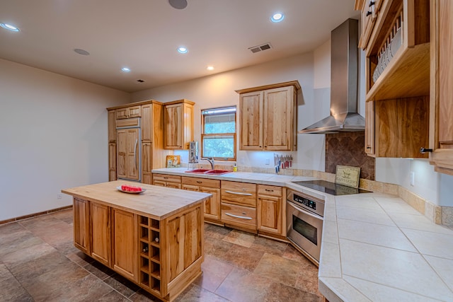 kitchen featuring stainless steel oven, black electric cooktop, wall chimney range hood, paneled built in refrigerator, and a center island