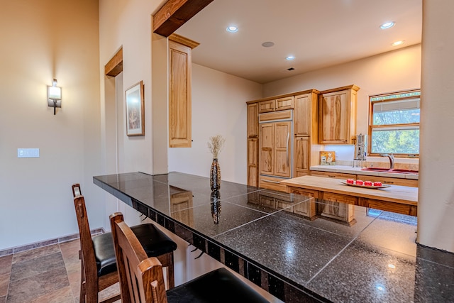 kitchen with a kitchen bar, light brown cabinetry, paneled refrigerator, kitchen peninsula, and sink