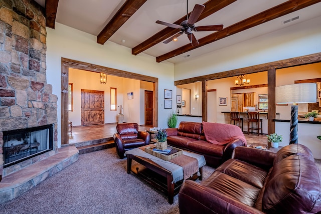 living room featuring beam ceiling, a stone fireplace, carpet floors, and ceiling fan with notable chandelier