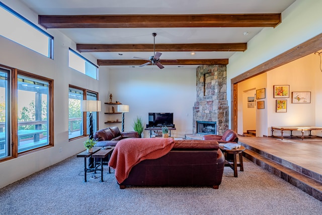 carpeted living room with beam ceiling, a stone fireplace, and ceiling fan