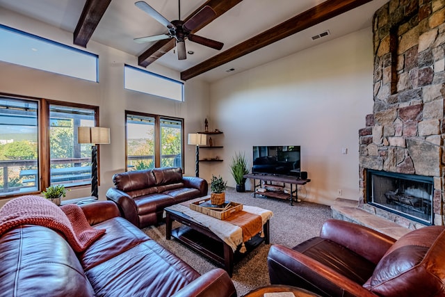 living room with a stone fireplace, carpet flooring, ceiling fan, a towering ceiling, and beamed ceiling