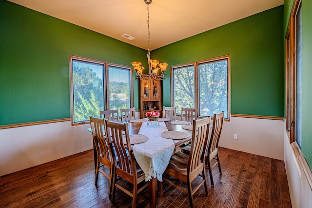 dining area with dark hardwood / wood-style floors, a wealth of natural light, and an inviting chandelier