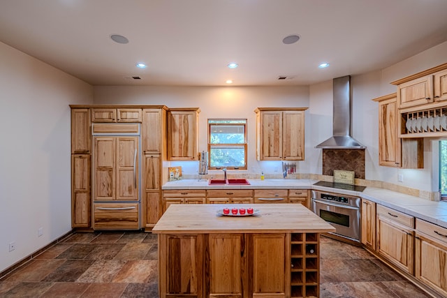 kitchen with paneled fridge, oven, wall chimney range hood, and a wealth of natural light