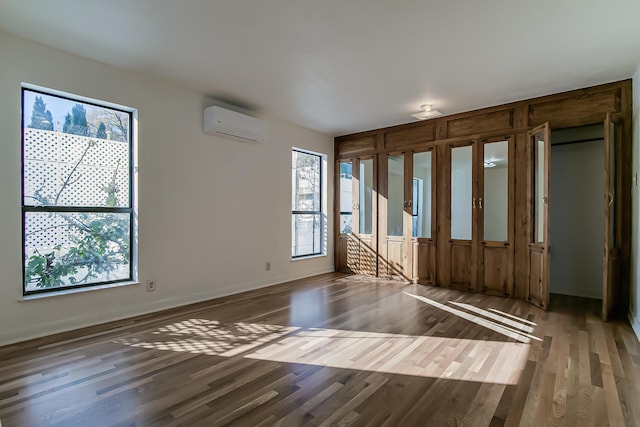 unfurnished room featuring plenty of natural light, dark hardwood / wood-style floors, and a wall mounted AC