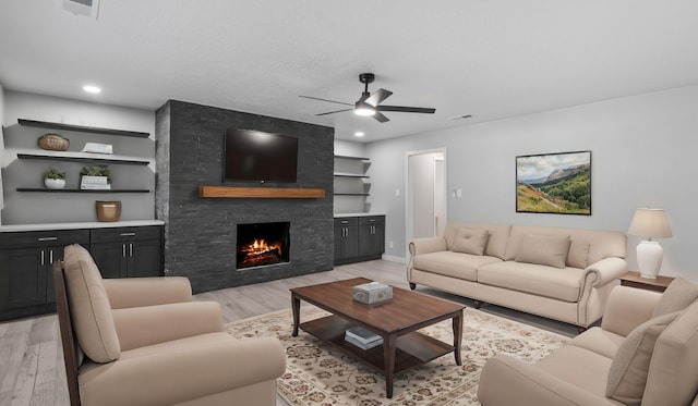 living room with ceiling fan, built in features, a textured ceiling, a fireplace, and light hardwood / wood-style floors