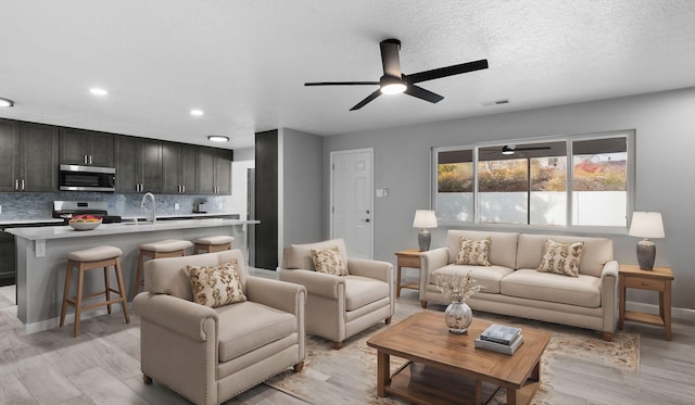 living room with a textured ceiling, light wood-type flooring, ceiling fan, and sink