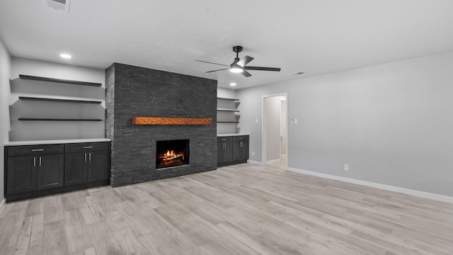 unfurnished living room featuring a textured ceiling, ceiling fan, a fireplace, and light hardwood / wood-style flooring