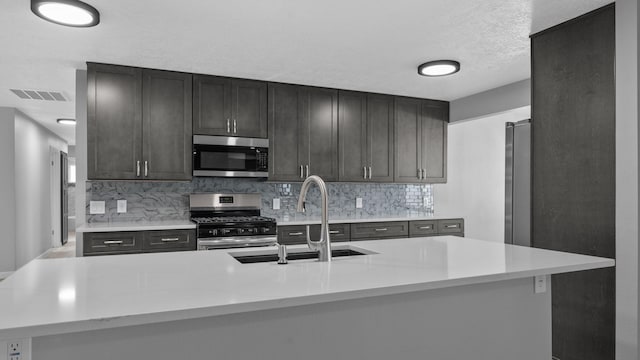 kitchen with sink, tasteful backsplash, light stone counters, a textured ceiling, and appliances with stainless steel finishes