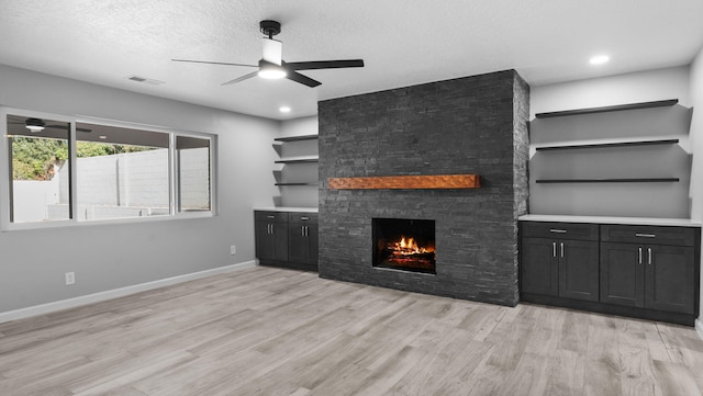 unfurnished living room with ceiling fan, a stone fireplace, light wood-type flooring, and a textured ceiling