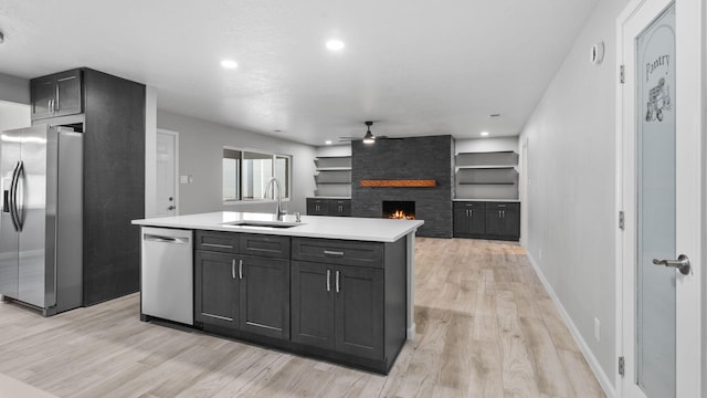 kitchen with built in shelves, sink, a stone fireplace, a kitchen island with sink, and appliances with stainless steel finishes