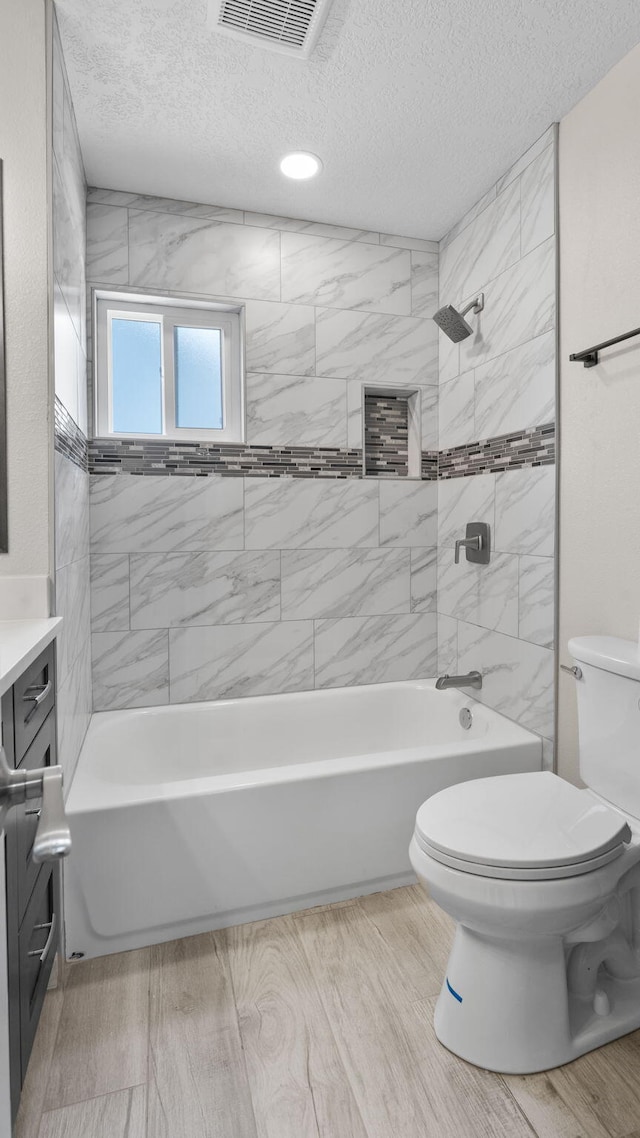 full bathroom featuring vanity, toilet, a textured ceiling, and tiled shower / bath