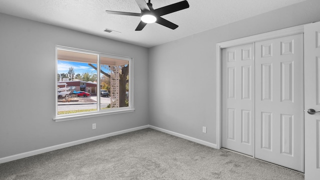 unfurnished bedroom with light carpet, a textured ceiling, a closet, and ceiling fan