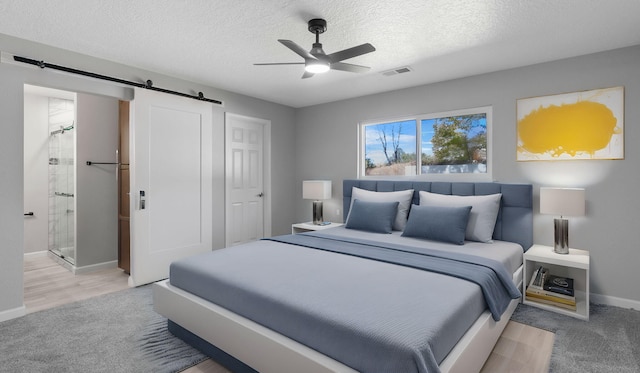 carpeted bedroom with connected bathroom, a barn door, ceiling fan, and a textured ceiling