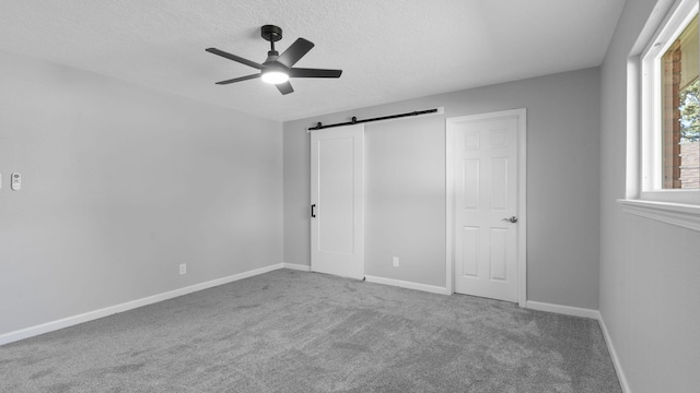 unfurnished bedroom featuring carpet flooring, a barn door, ceiling fan, and a textured ceiling