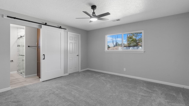 unfurnished bedroom featuring a textured ceiling, ceiling fan, a barn door, and light carpet