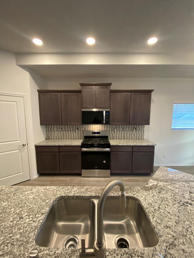 kitchen with stainless steel appliances, dark brown cabinetry, light stone countertops, sink, and tasteful backsplash