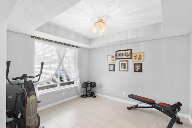 workout area featuring a chandelier, a raised ceiling, and a textured ceiling