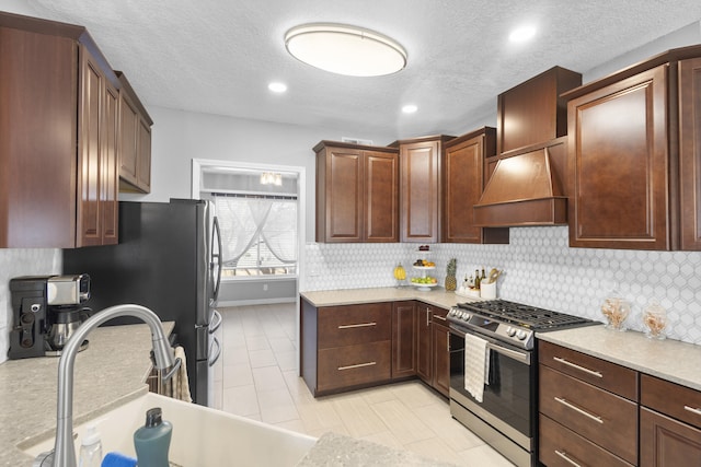 kitchen featuring premium range hood, tasteful backsplash, sink, stainless steel range with gas stovetop, and a textured ceiling