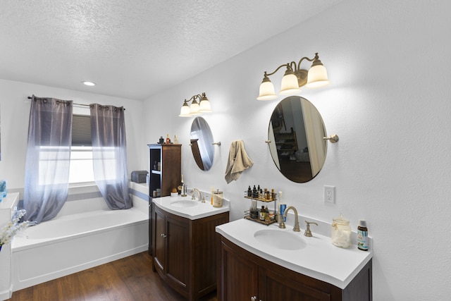 bathroom with wood-type flooring, a bathing tub, vanity, and a textured ceiling