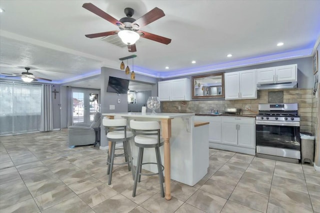 kitchen featuring decorative backsplash, gas range, white cabinetry, a kitchen island, and a breakfast bar area