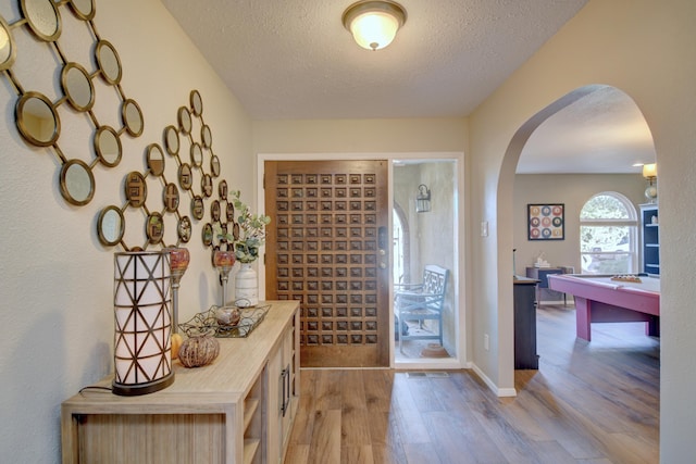 foyer with baseboards, wood finished floors, arched walkways, and a textured ceiling