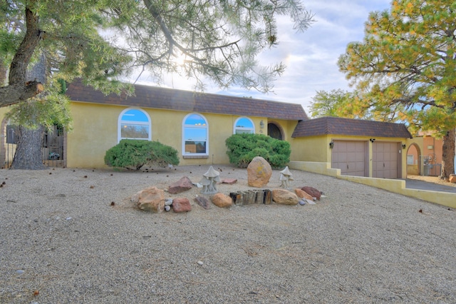 view of front facade featuring an attached garage, a shingled roof, stucco siding, mansard roof, and driveway