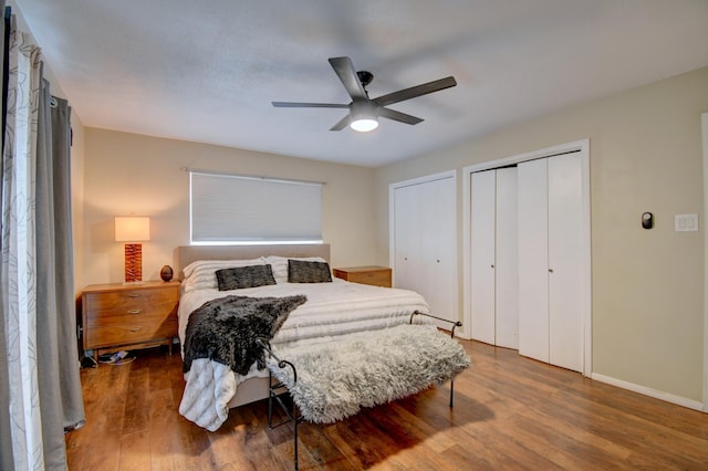 bedroom featuring baseboards, two closets, wood finished floors, and a ceiling fan