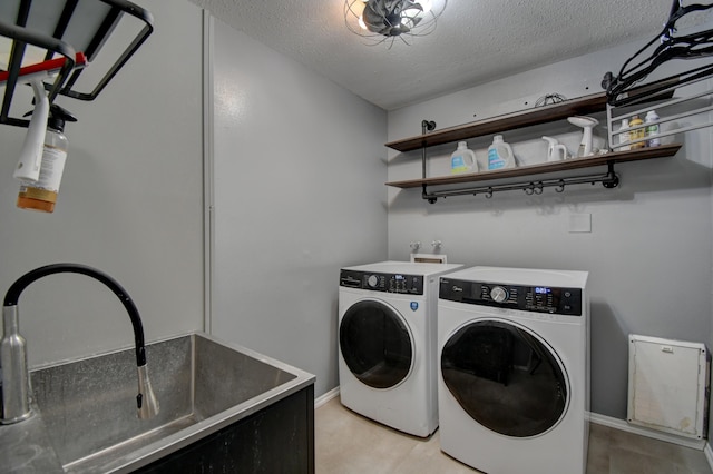 laundry room featuring washing machine and clothes dryer, laundry area, a textured ceiling, and a sink