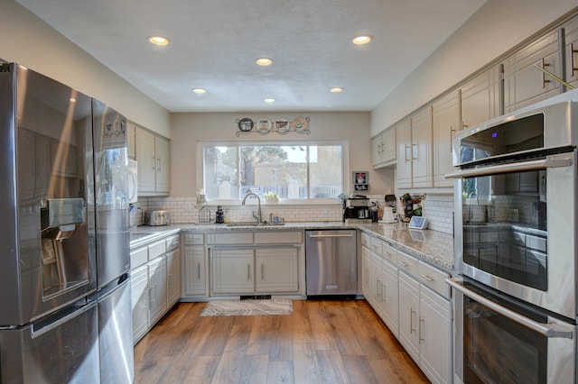 kitchen with light stone countertops, light wood finished floors, a sink, decorative backsplash, and stainless steel appliances